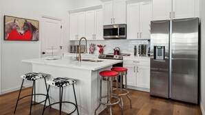 A modern kitchen with white cabinets, stainless steel appliances, and a central island with stools. - Walk to the Arlington stadiums from this Luxurious Condo w/ Premium Amenities! Rooftop Retreat w views of stadiums, private garage, gourmet kitchen & gated entry. Book Now to stay at the New Ruby Lux Skyline Retreat  in the Heart of the Arlington! (ARLINGTON)