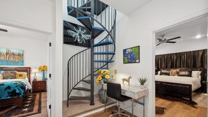 A bedroom with a bed, a desk, a chair, a staircase, and a ceiling fan.