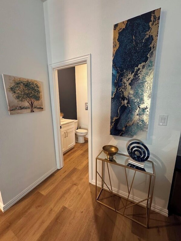 A hallway with a wooden floor, a white door leading to a bathroom, and a large abstract painting on the wall.