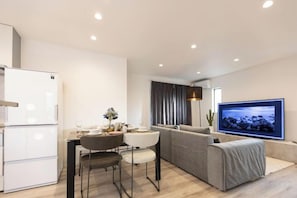 A modern living room with a sofa, a dining area with a table and chairs, a flat-screen TV mounted on the wall, and a kitchen area with a refrigerator. - JS xiaozhai・Hoshishiro 1A (Osaka)