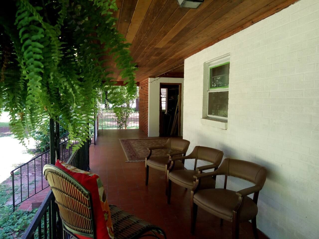 Un portico coperto con due poltrone in pelle marrone, una poltrona in vimini e un cuscino rosso.