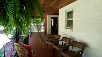 Un portico coperto con due poltrone in pelle marrone, una poltrona in vimini e un cuscino rosso.