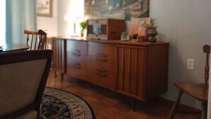 A dining area with a wooden table and chairs, a patterned rug, and a wooden cabinet with drawers.
