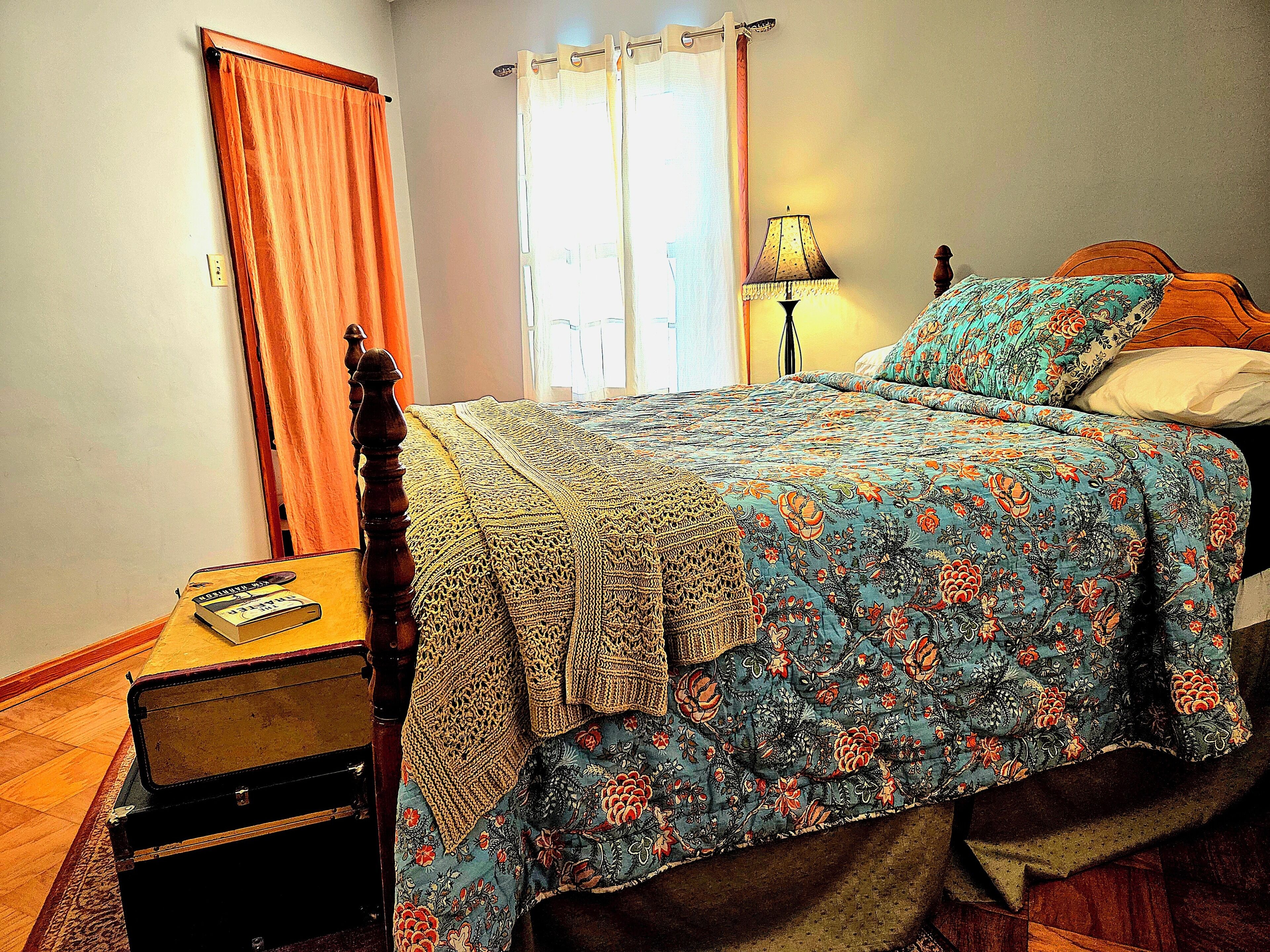 A bedroom with a bed, a nightstand, a lamp, and a suitcase.