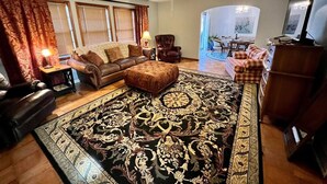 A living room with a large patterned rug, leather sofas, a ceiling fan, and a dining area with a table and chairs.