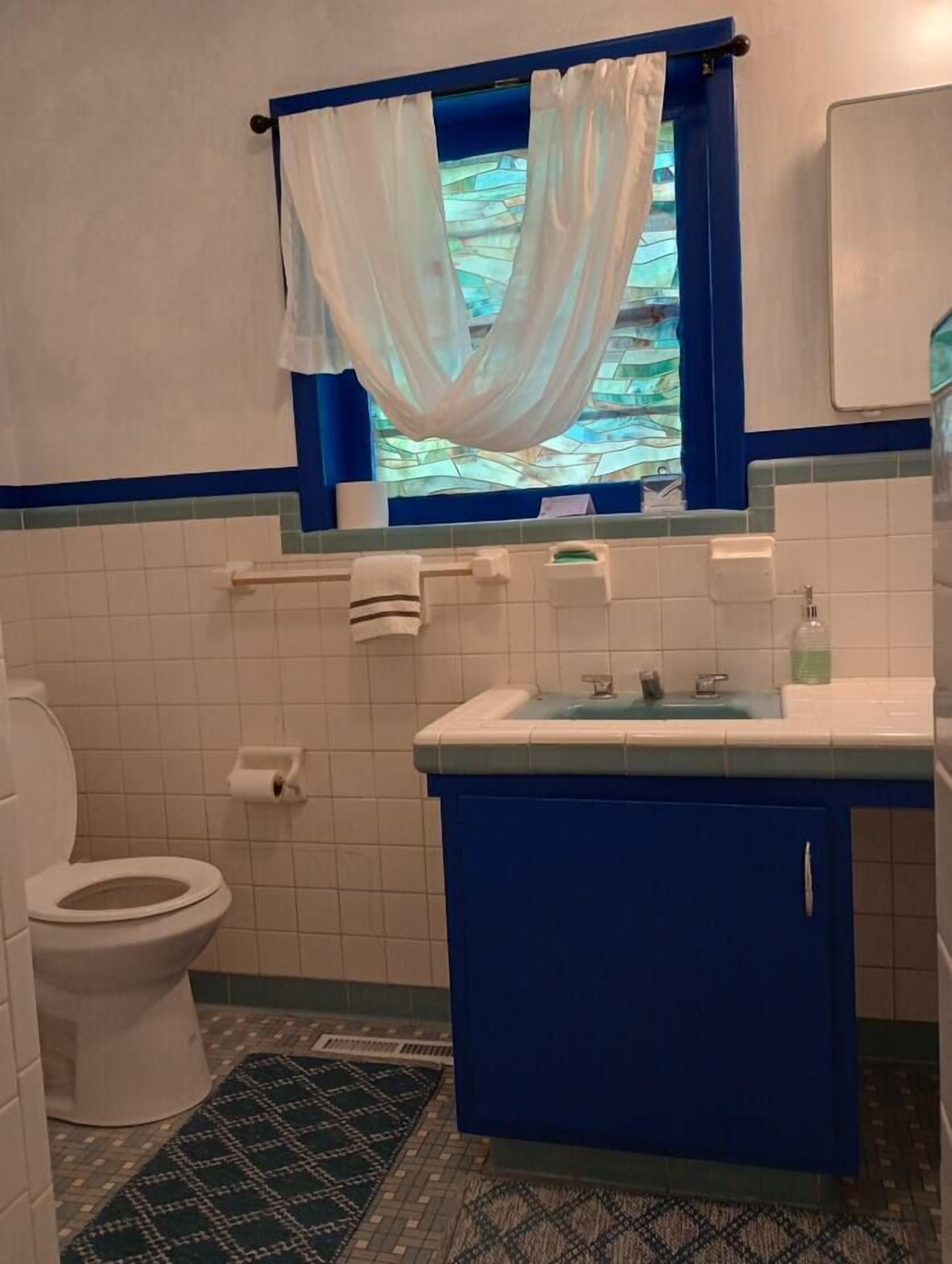 A bathroom with a toilet, a sink, and a window with a curtain.