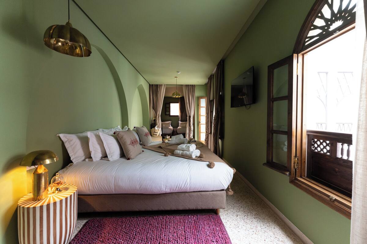 A bedroom with a bed, a nightstand, a lamp, and a window with curtains.