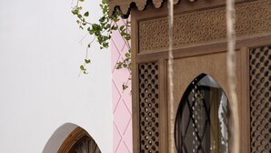 Una ventana de madera tradicional con tallas intrincadas y un patrón geométrico rosa en la pared.