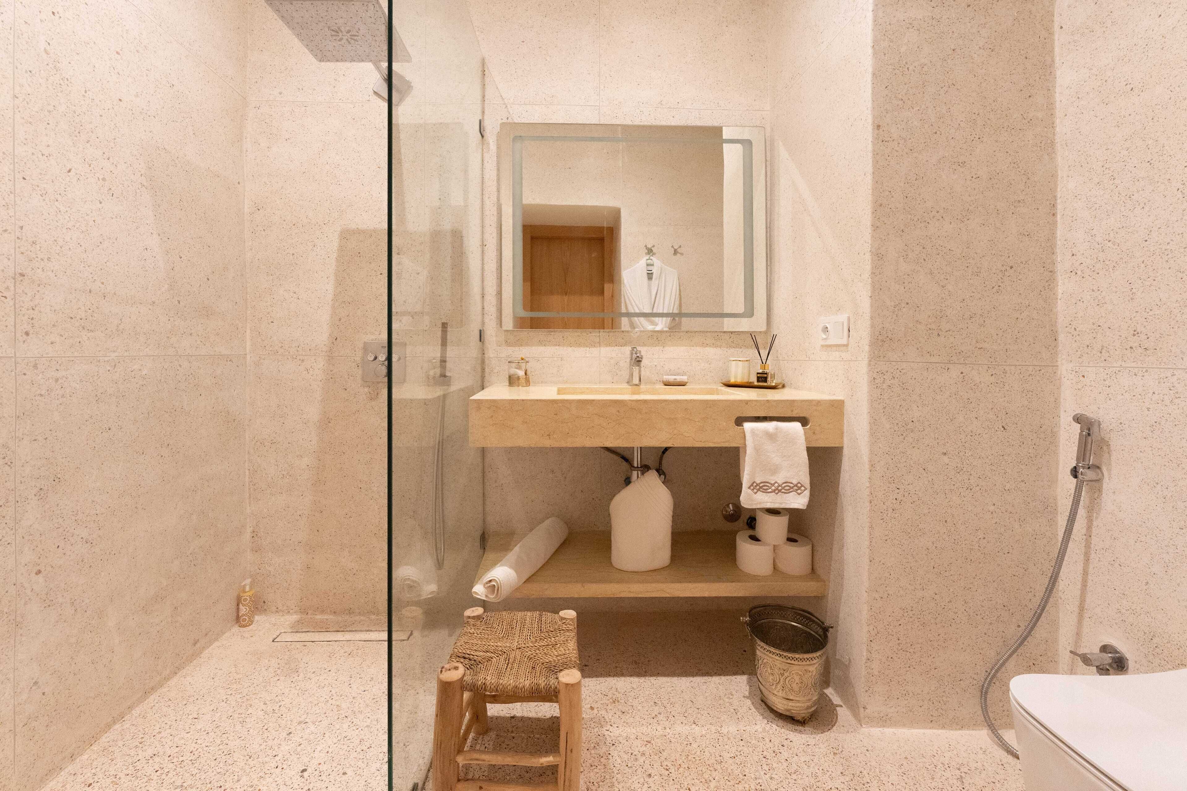 A modern bathroom with a glass shower enclosure, a wooden stool, a sink with a towel, and a toilet.