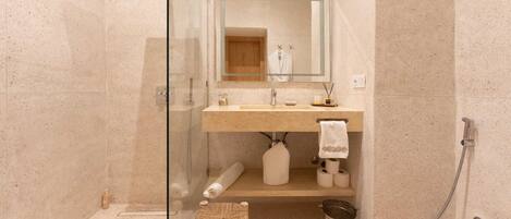 A modern bathroom with a glass shower enclosure, a wooden stool, a sink with a towel, and a toilet.