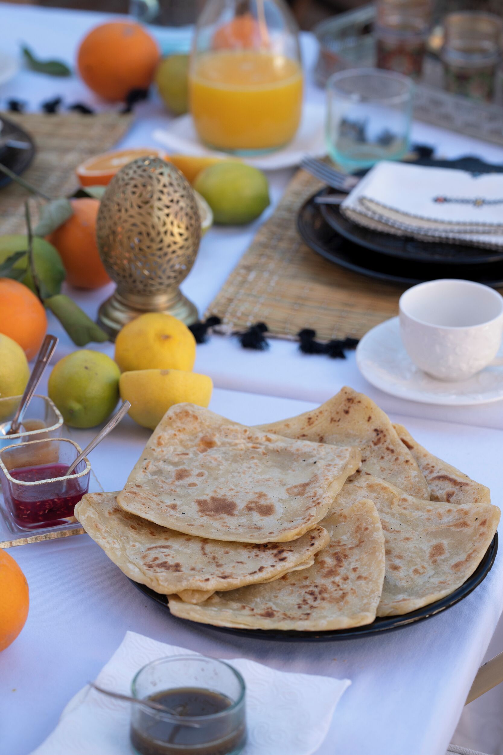 A table set with flatbreads, fruits, a jug of orange juice, and a cup of tea.