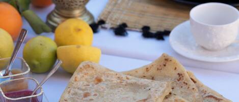 A table set with flatbreads, fruits, a jug of orange juice, and a cup of tea.