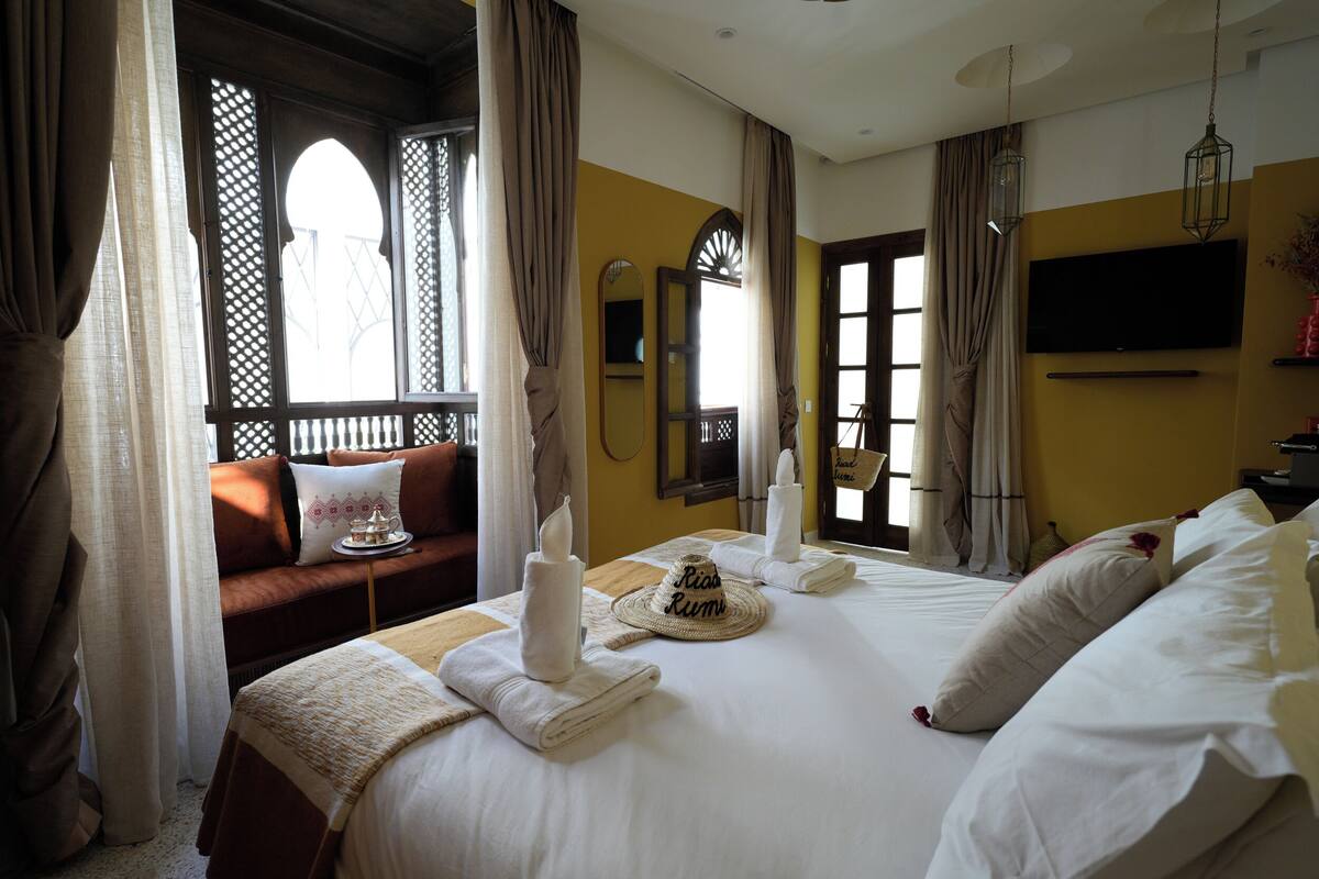 A hotel room with a bed, a sofa, a TV, and a window with curtains.