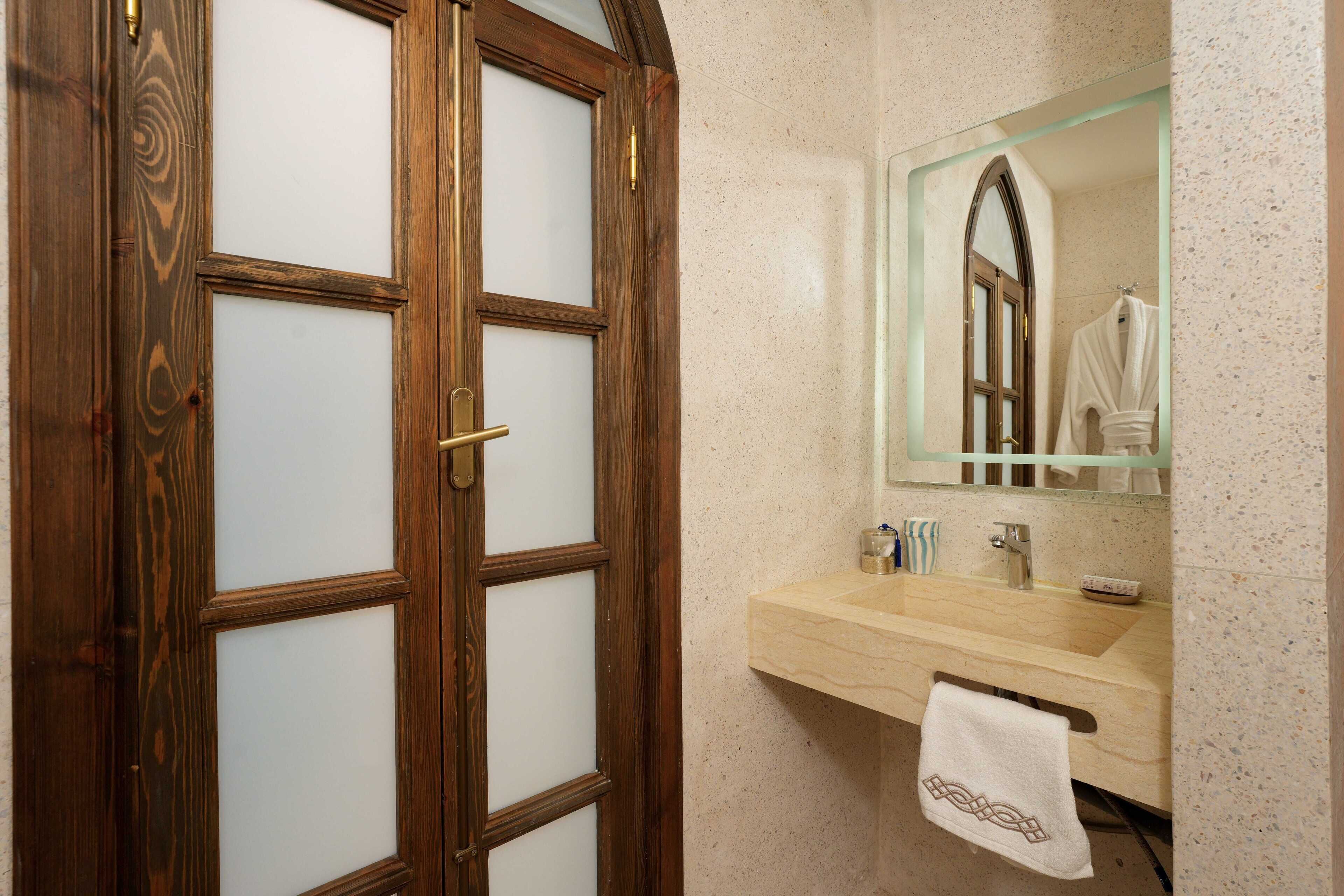 A bathroom with a wooden door, a mirror, a sink, and a towel hanging on the wall.