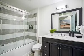 A modern bathroom with a glass shower enclosure, a white toilet, a black vanity with a mirror, and a small potted plant.