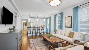 Un salon moderne comprenant un canapé, une table basse et des fauteuils, un coin cuisine avec des tabourets de bar et une table à manger.