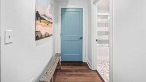 Un couloir avec une porte bleue, un banc en bois et un tableau accroché au mur.