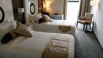 Camera d'albergo con due letti, un comodino, una sedia e un'ampia finestra.