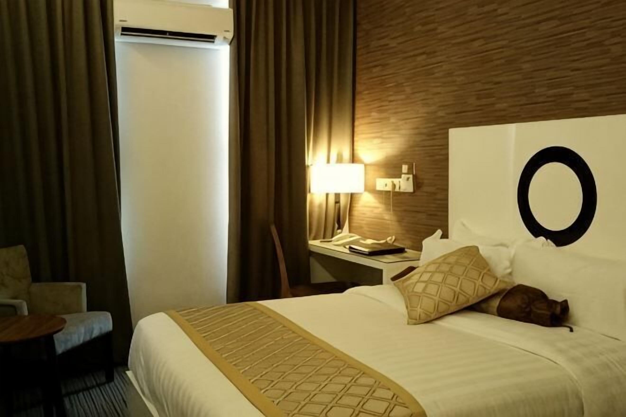Una habitación de hotel con una cama, una mesita de noche con lámpara, una silla y un perchero.