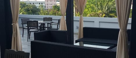 An outdoor seating area with a table and chairs, surrounded by dark wicker furniture, and beige curtains.