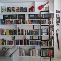 Una estantería llena de libros y marcos con fotografías, una guitarra roja y un cartel de prohibido fumar.
