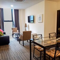 Habitación de hotel con sofá, sillones, mesa de comedor con sillas, televisor y un cuadro en la pared.