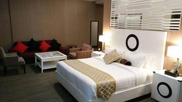 Una camera d'albergo con un letto, un angolo salotto con divano e poltrone, un tavolino e un comodino con lampada.