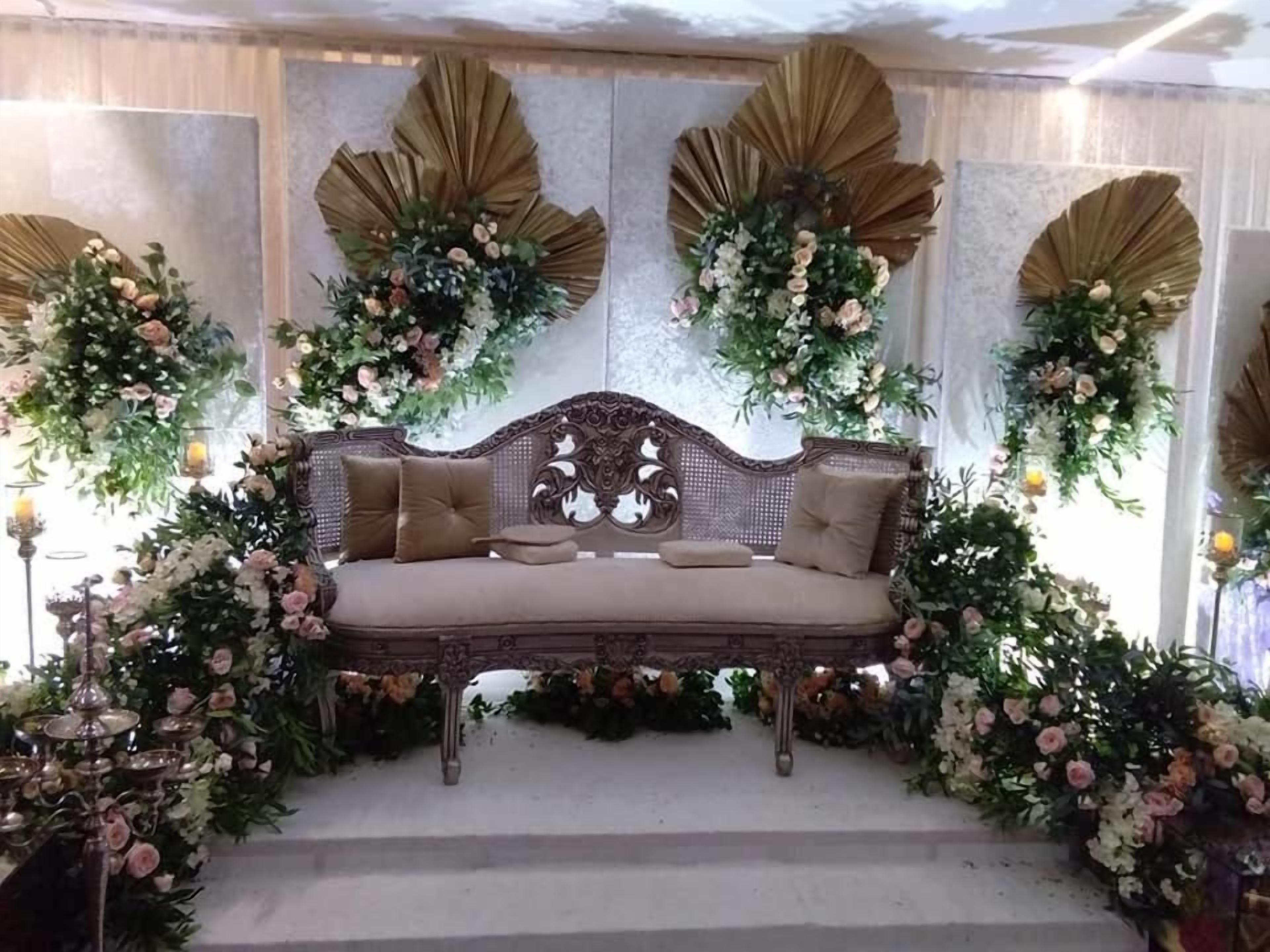 Un canapé doté d’un dossier décoratif, entouré d’arrangements floraux et d’éléments décoratifs muraux.