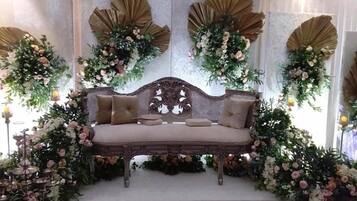 Un canapé doté d’un dossier décoratif, entouré d’arrangements floraux et d’éléments décoratifs muraux.