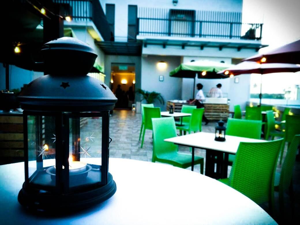 An outdoor seating area with green chairs and tables, a lantern, and a building in the background.