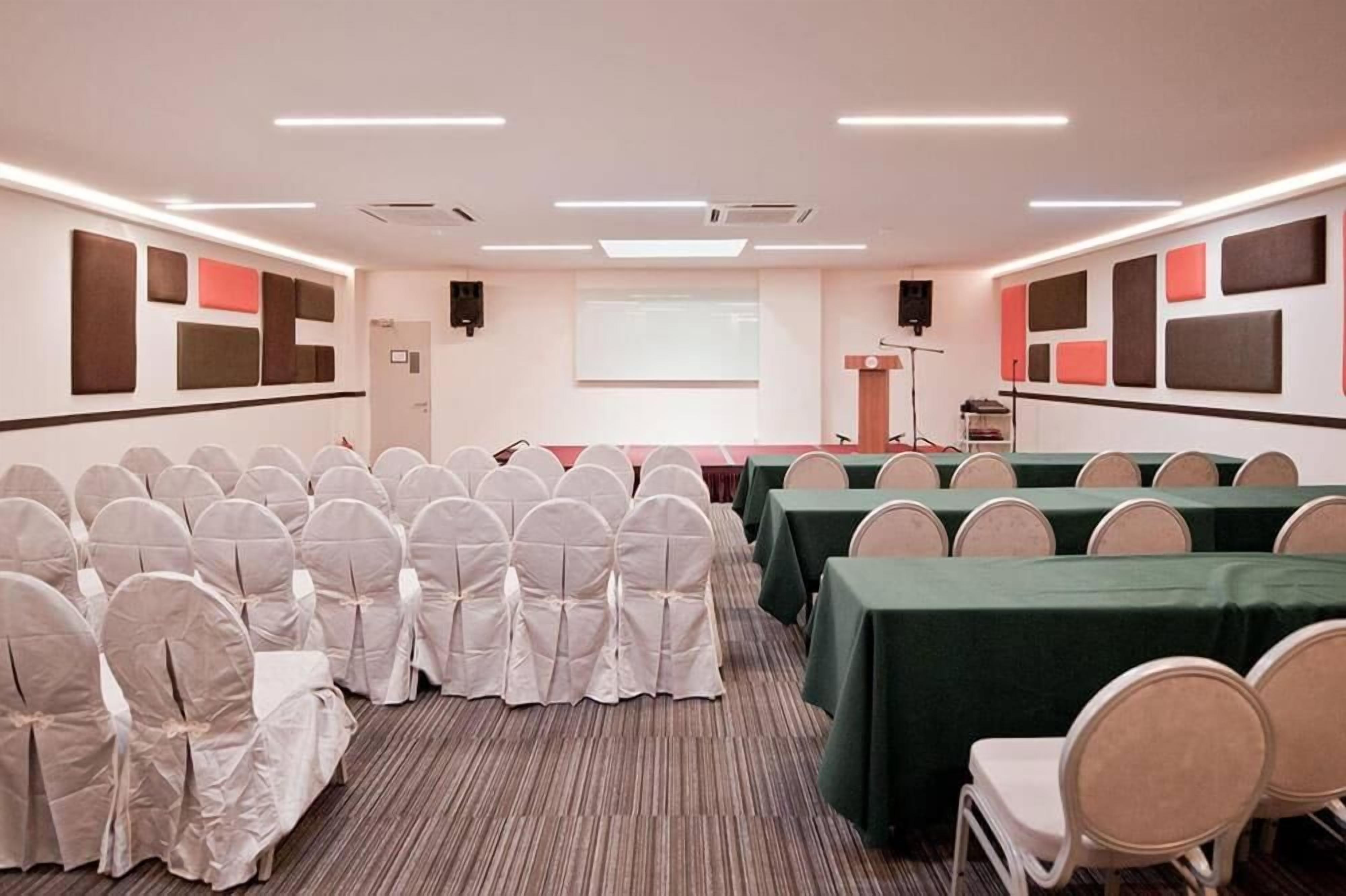 A conference room with rows of chairs, a projector screen, and tables with green tablecloths.