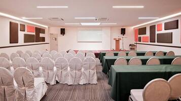 A conference room with rows of chairs, a projector screen, and tables with green tablecloths.