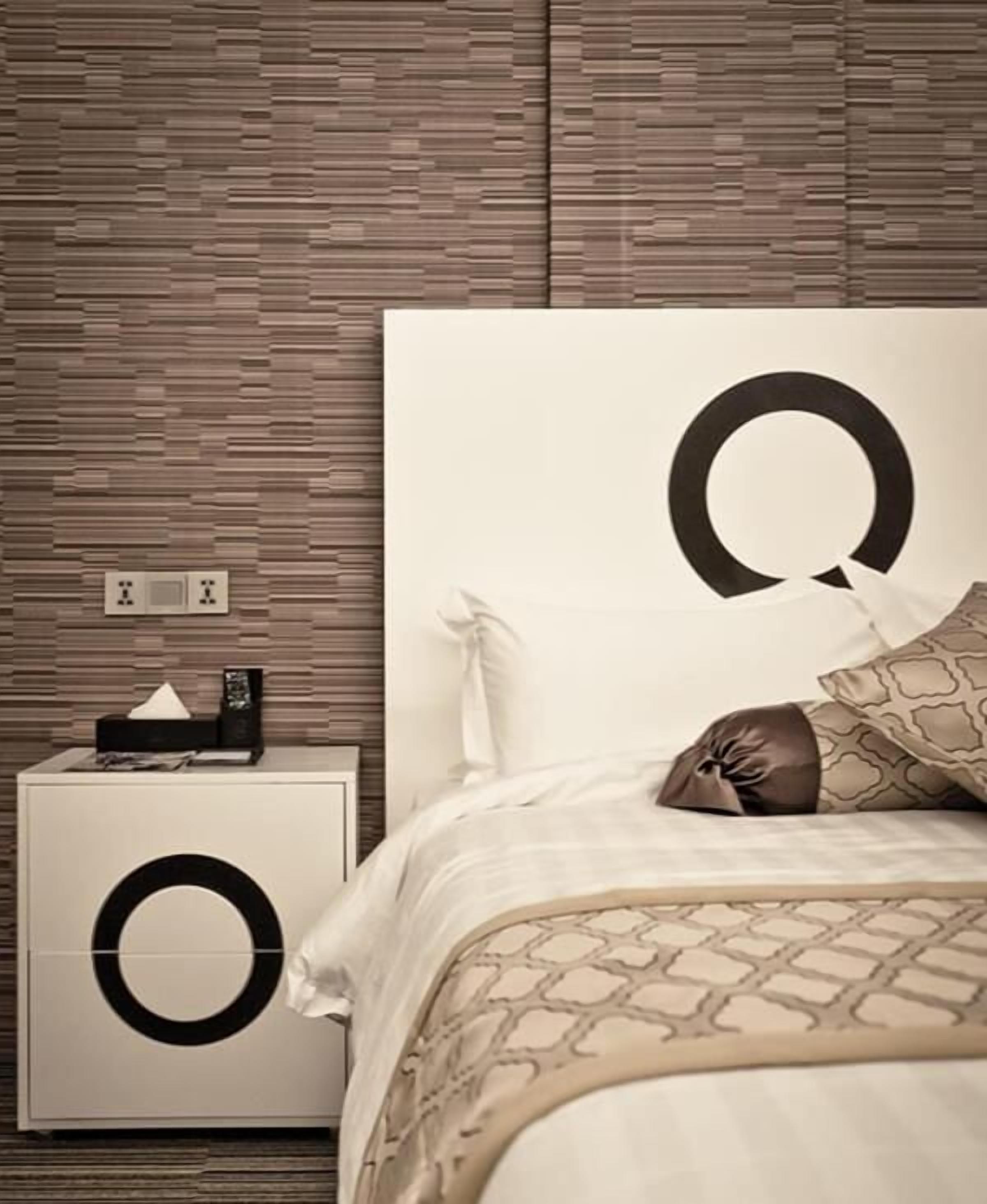 Quarto moderno com uma cama grande, uma mesa de cabeceira com um estojo de lenços e uma parede com design em painel de madeira.