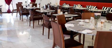 Un restaurant avec plusieurs tables et chaises, un mur rouge et noir, et des tableaux encadrés accrochés au mur.