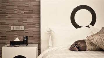 Une chambre moderne avec un grand lit, une table de chevet avec un boîte de mouchoirs, et un mur orné d’un panneau en bois.