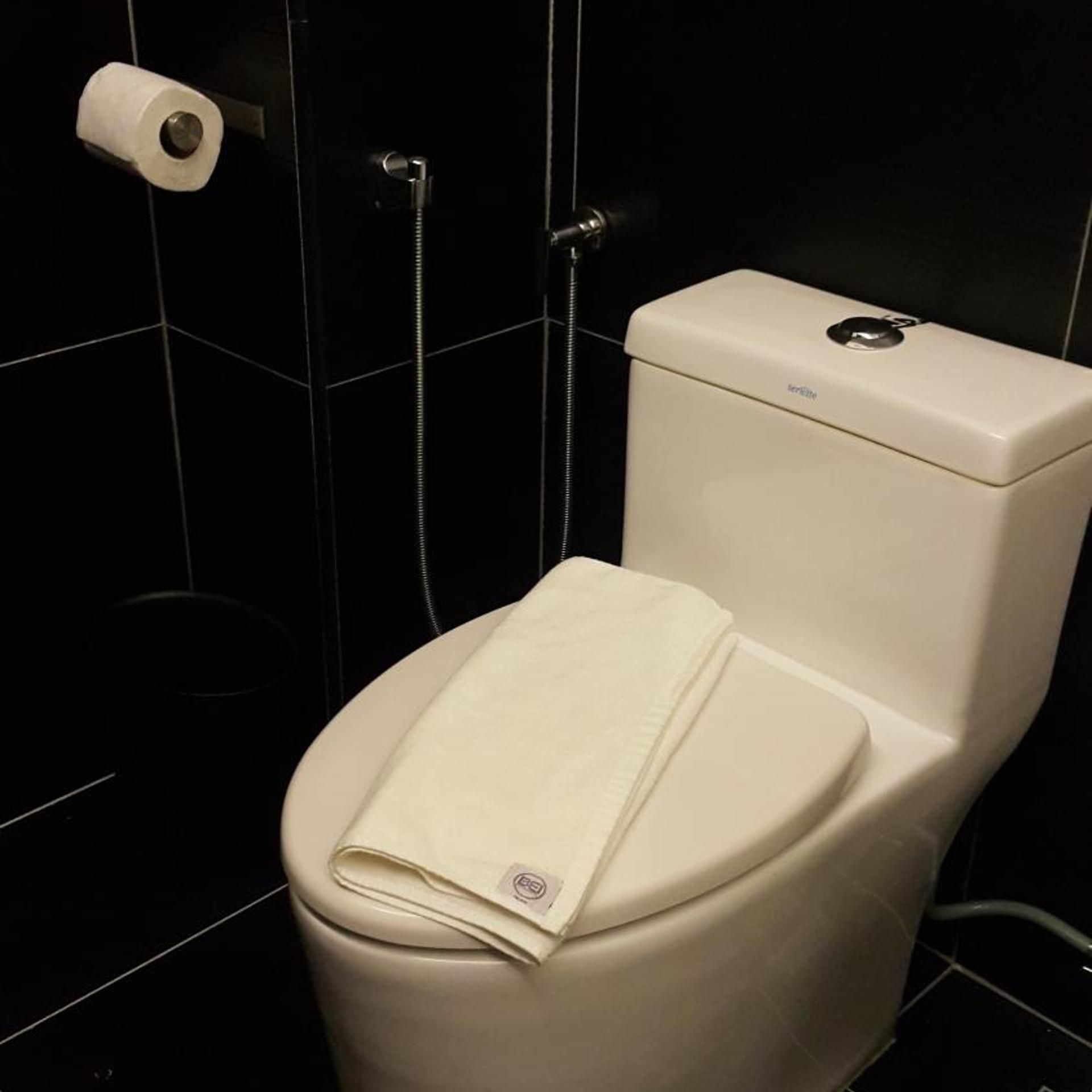 Un inodoro con una toalla encima, un rollo de papel higiénico y un cabezal de ducha.