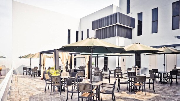Ein Außenbereich mit einer Terrasse, mehreren Tischen und Stühlen, Sonnenschirmen und einem modernen Gebäude im Hintergrund.