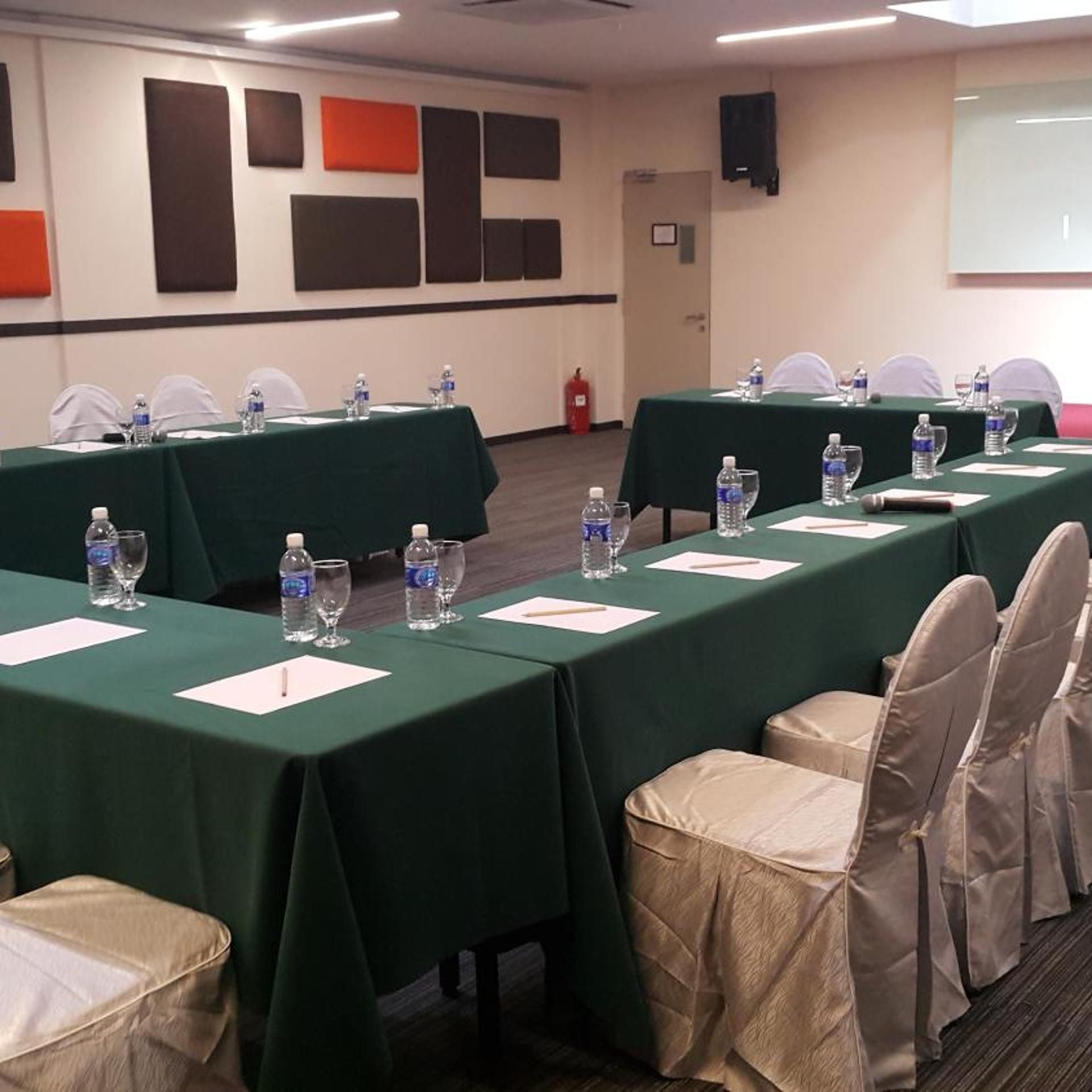 Una sala conferenze con tavoli apparecchiati per una riunione, dotata di bottiglie d'acqua e bicchieri.