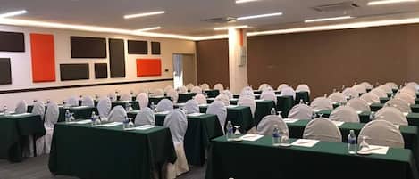 A conference room with rows of tables, each with a water bottle, glass, and notepad.