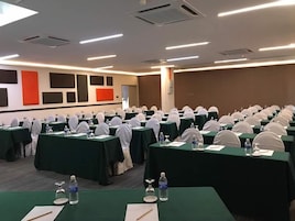Un salón de conferencias con filas de mesas, cada una con una botella de agua, un vaso y un bloc de notas.