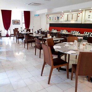 A restaurant with multiple tables and chairs, a red and black wall, and framed pictures on the wall. - Bei Boutique Hotel (Muar)