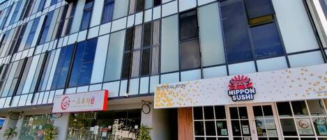 A modern building with a glass facade, a restaurant named 'NIPPON SUSHI' on the ground floor, and a sign for 'RESTORAN JAPON' above the entrance.