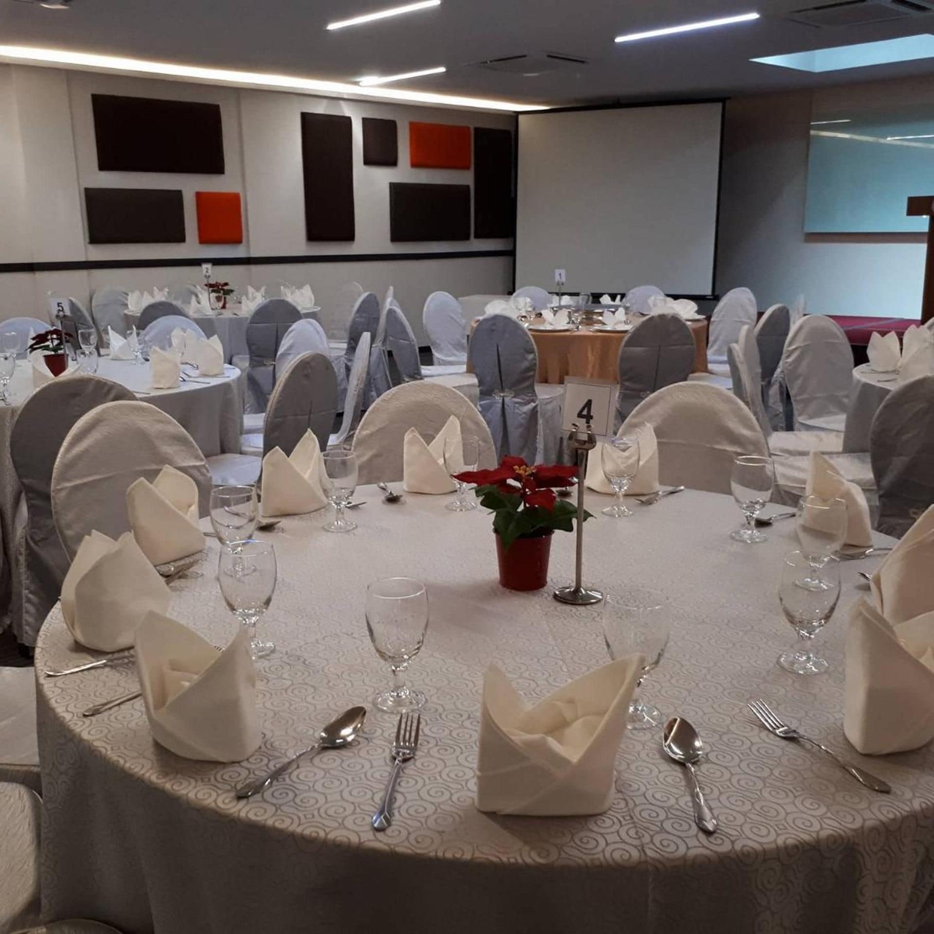 Una sala conferenze con tavoli rotondi, tovaglie bianche e sedie rivestite di bianco.