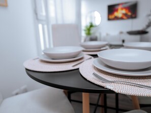 Una mesa de comedor con platos blancos y cubiertos, sobre una mesa negra con individuales tejidos.
