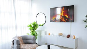 A modern living room with a grey armchair, a round table, a white cabinet with candles, and a fireplace painting.