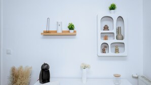 A minimalist room with a white wall, a wooden shelf with decorative items, a white console table with a vase and a small plant, and a radiator.
