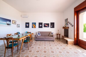 Een woonkamer met een glazen eettafel, houten stoelen, een bank en een open haard.