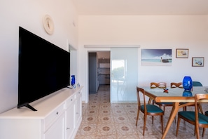 Un salon avec un téléviseur, une table à manger, des chaises et une cuisine à l’arrière-plan.