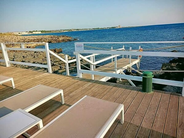 A wooden deck with white railings overlooking a rocky shoreline and the sea.