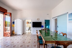 Een eethoek met een glazen tafel, houten stoelen, een televisie en vloerbedekking met een patroon.